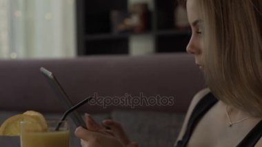 Cam suyu ile kanepede oturan ekran tablet bilgisayar kullanan genç kadın