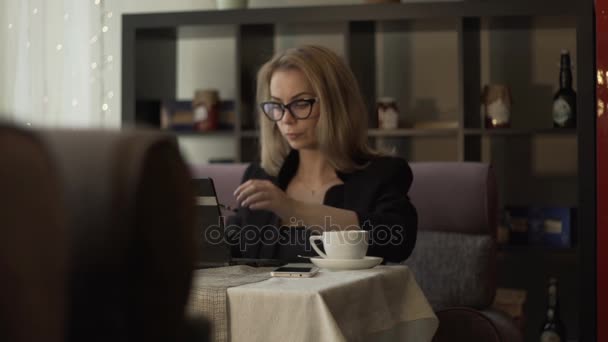 Joven mujer de negocios en gafas de escribir en el teclado portátil en el sofá en la cafetería — Vídeos de Stock