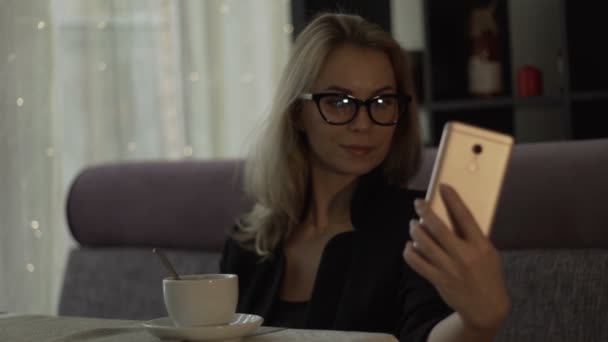 Mujer joven en gafas haciendo selfie en el teléfono móvil durante el almuerzo en la cafetería de moda — Vídeos de Stock