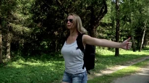 Young woman traveler with backpack hitchhiking on road on summer day — Stock Video