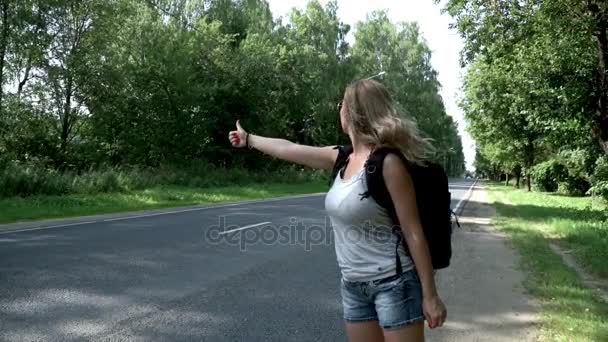 Hitchhiking woman traveler with backpack standing on road on summer day — Stock Video