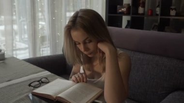 Genç kadın rahat kanepede kafede masada oturan bir kitap okuma