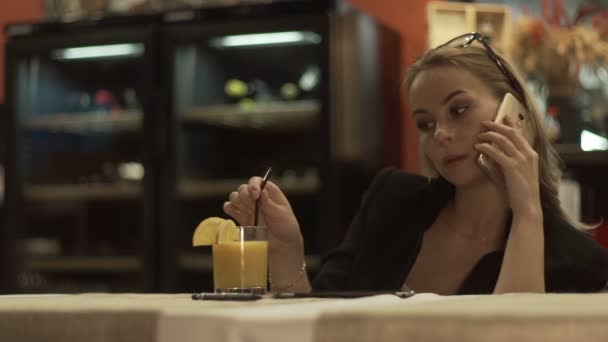 Деловая женщина звонит по мобильному телефону и пьет апельсиновый сок из стекла — стоковое видео