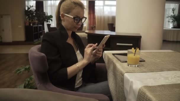 Femme moderne dans des lunettes en utilisant le téléphone mobile sur fond intérieur café de luxe — Video