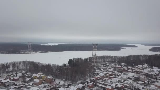 Electric torn med kraftledningar stående på floden stranden i winter village Flygfoto. Drone överföring torn med kraftledningar på vinterlandskap. — Stockvideo