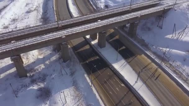 Schorsing treinbrug boven winter snelweg en auto verkeer op besneeuwde weg luchtfoto landschap. Drone weergave trein brug en auto verplaatsen op snelweg weg. — Stockvideo