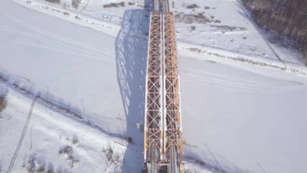 Train à vue de drone se déplaçant sur le pont ferroviaire sur la rivière d'hiver. Trafic ferroviaire sur un pont suspendu à travers un paysage aérien gelé . — Video