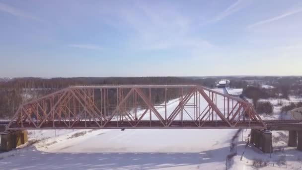Felfüggesztés vasúti híd alatt téli folyó légifelvételek vonat mozgását. Téli vasúti hídon át fagyasztott river drone megtekintése. — Stock videók