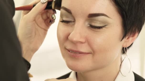 Cerrar la cara de la mujer durante la aplicación de maquillaje cosmético con cepillo en la piel en el salón de belleza. Retrato hermosa mujer mientras que la cara maquillaje en salón de cosméticos . — Vídeo de stock