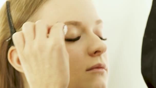 Kvinna visagiste använda kosmetika svamp för make up ansikte ung kvinna i skönhetsstudio. Närbild av ung kvinna modell under makeup ansikte i skönhet skola. — Stockvideo