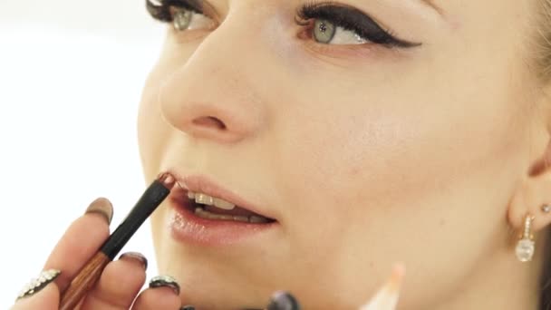 Χέρι καλλιτέχνης μακιγιάζ με χείλη ζωγραφική καλλυντικά βούρτσα στο πρόσωπο της γυναίκας. Μακιγιάζ χειλιών εσωτερικη — Αρχείο Βίντεο