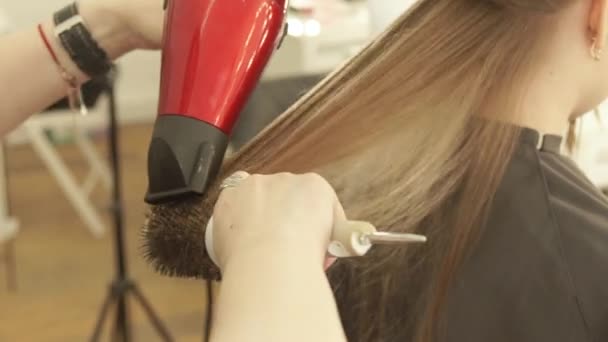 El peluquero que seca el cabello femenino después de la peluquería en el salón de belleza. Cerrar corte de pelo peinado pelo largo con secador y cepillo después de lavar y cortar. Terminar la peluquería en el salón de belleza . — Vídeos de Stock