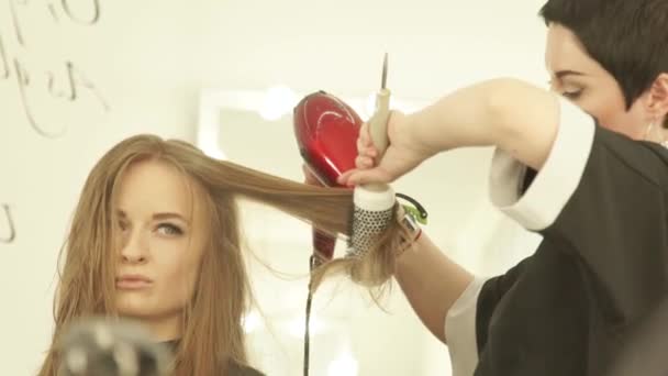 Mooie vrouw tijdens hairstyling lange haren met droger en haarborstel in de schoonheidssalon. Close-up van haarkapper Droogrek vrouw met droger en kam na het wassen en snijden in de kapsalon. — Stockvideo