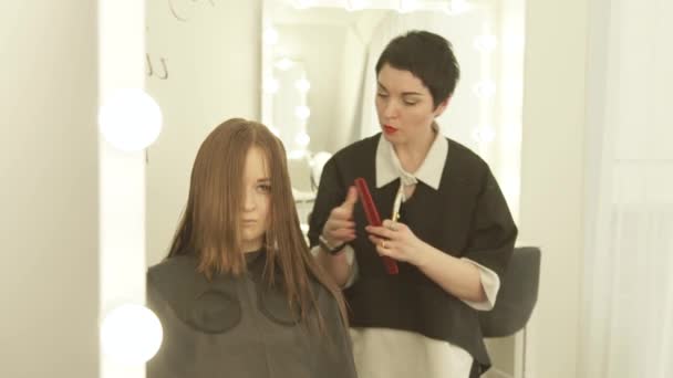 Перукар розчісує і ріже довге волосся ножицями в перукарні. Крупним планом перукар робить жінку зачіска з ножицями в студії краси . — стокове відео