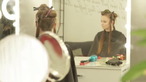 Молода жінка з застібкою для фіксації довгого волосся під час перукарень, сидячи в передньому дзеркалі стільця в студії краси. Жіноча модель волосся в салоні фентезі . — стокове відео