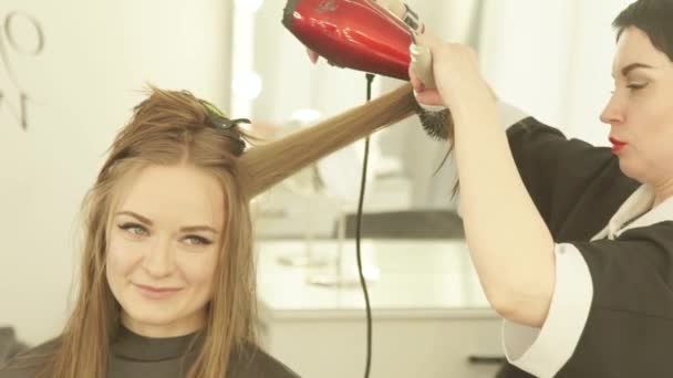 Coiffeur faisant coiffure femme cheveux longs avec sèche-cheveux et brosse dans le salon de beauté. Fermer coupe-cheveux sèche-cheveux femme avec sèche-cheveux et brosse à cheveux après le lavage et la coupe dans le salon de coiffure . — Video