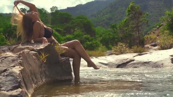 Mulher despreocupada de biquíni sentado em uma pedra no rio da montanha no verão . — Vídeo de Stock