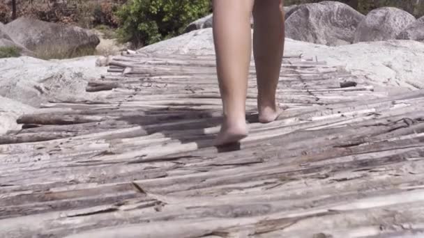 Cerca de mujer descalza caminando a lo largo de un puente de madera en la montaña pedregosa . — Vídeo de stock