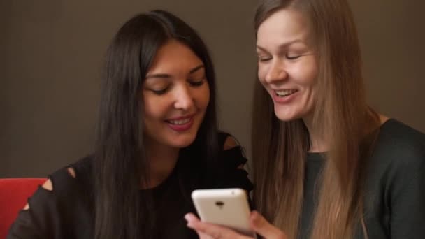 Dos chicas lindas se sientan en un café ver fotos en el teléfono, reír y hablar sobre el café — Vídeos de Stock