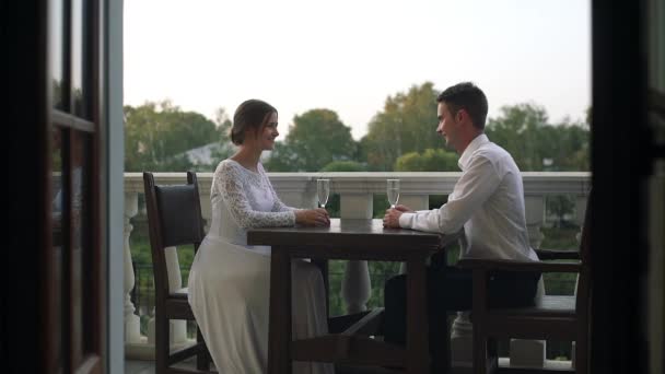 Beautiful loving couple sitting at a table in a restaurant outdoors on their wedding day. — Stockvideo