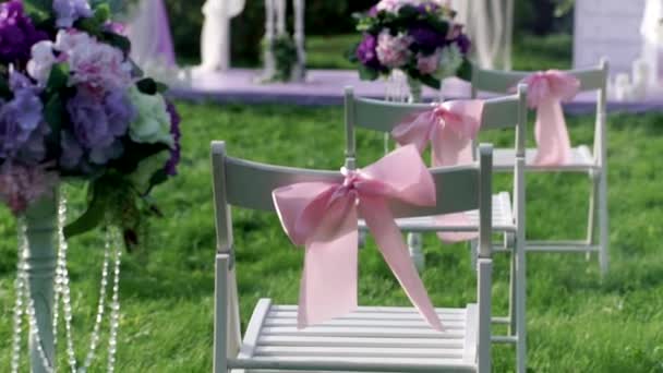 Las sillas blancas con lazos rosados se cierran al aire libre en el verinke de boda. Decoraciones de boda . — Vídeo de stock