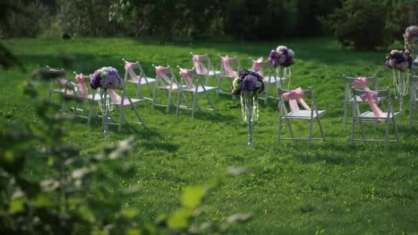 Weiße Stühle mit rosa Schleifen und ein Traualtar in Weiß und Lavendelfarben. — Stockvideo