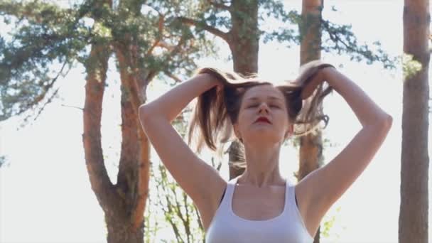 Schöne traurige Mädchen mit roten Lippen spielen mit ihren langen braunen Haaren im Wald. — Stockvideo