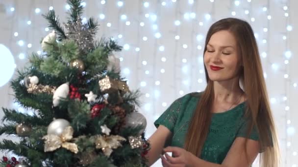 Retrato de una hermosa mujer sexy con lápiz labial rojo viste el árbol de Navidad, admirando los juguetes, sonrisas lindas — Vídeo de stock