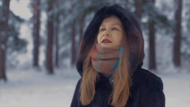 Beautiful girl standing in a snowy pine forest and looks around — Stock video