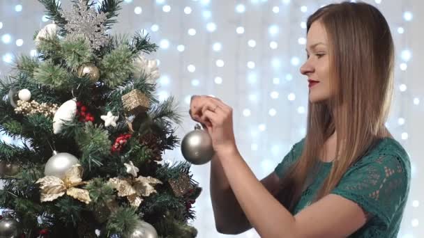 Schöne modische Mädchen in einem grünen Kleid mit roten Lippen schmückt den Weihnachtsbaum — Stockvideo