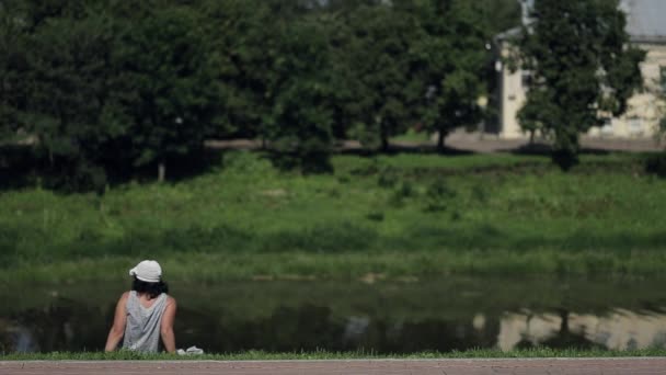 Femme adulte au panama assise sur la rive de la rivière, au repos, respirant de l'air — Video