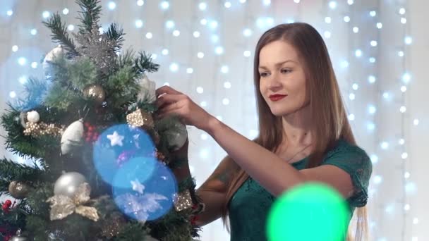 Όμορφη σέξι γυναίκα με κόκκινο κραγιόν φορέματα μέχρι το χριστουγεννιάτικο δέντρο, χαριτωμένα χαμόγελα, ισιώνει παιχνίδια, Απολαύστε τη διαδικασία — Αρχείο Βίντεο