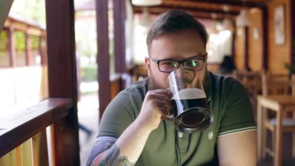 Getatoeëerd, bebaarde man zit aan de bar op de zomer veranda — Stockvideo