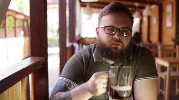 Tetovaný vousatý muž sedí u baru na verandě letní — Stock video