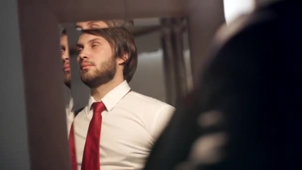 Brutale bebaarde man gekleed in een mooie trouwdag. De bruidegom draagt een rode stropdas in de reflectie van een spiegel jas — Stockvideo
