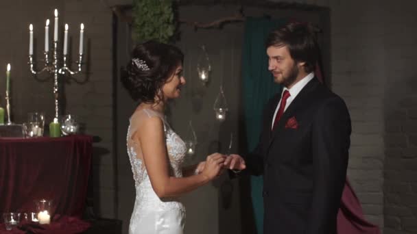 De bruid draagt een trouwring aan de bruidegom op een fantastische locatie met kaarsen — Stockvideo