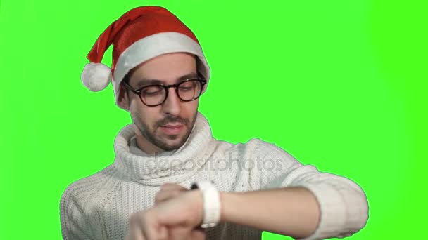 Brutal homem sério em um boné de Papai Noel usando smartwatch tela de toque em um fundo verde — Vídeo de Stock