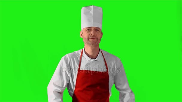 Handsome adult chef turns, he crosses his arms with knives and nods his head on a green background — Stock Video