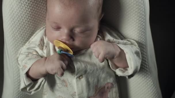 A charming baby with pacifier in his mouth sleeping on the bed. — Stock Video