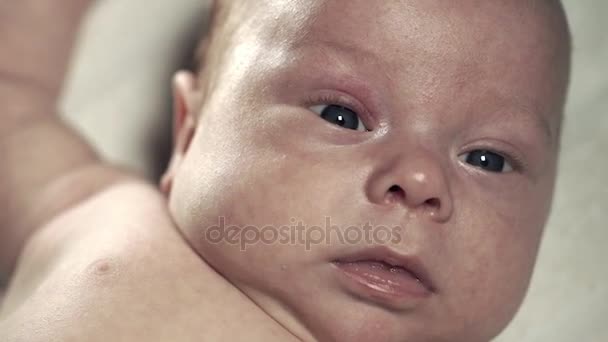 Een schattige baby op het bed ligt en actief beweegt. Gezicht close-up — Stockvideo