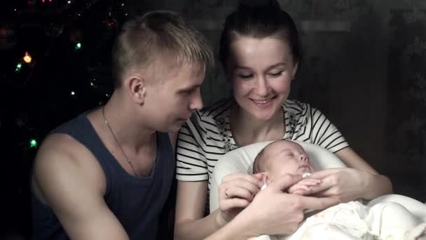 Los padres jóvenes miran al bebé y le acarician la mano. Año Nuevo interior — Vídeos de Stock