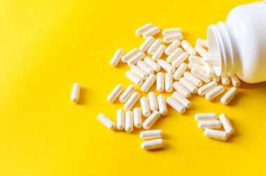 Bir grup beyaz tablet. Sarı şişeden kapsüller dökülüyor. Kırmızı arka plan. Yol konsepti.