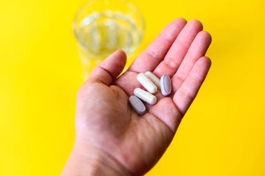 Sarı arka planda bir bardak su ve kapsül hapı.