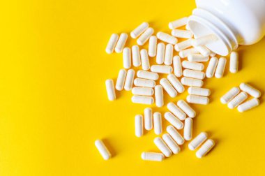 Bir grup beyaz tablet. Sarı şişeden kapsüller dökülüyor. Kırmızı arka plan. Yol konsepti.