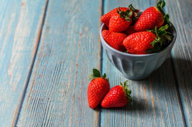 Mavi ahşap arka planda mavi bir kasede duran güzel organik çilekler..