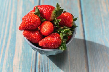 Mavi ahşap arka planda mavi bir kasede duran güzel organik çilekler..