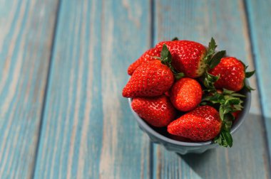 Mavi ahşap arka planda mavi bir kasede duran güzel organik çilekler..