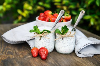 Ahşap bir masada chia ile iki bardak yoğurt nane ve çilekle süslenir..
