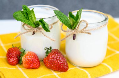 Nane ve çilekle süslenmiş beyaz arka planda iki bardak doğal yoğurt..