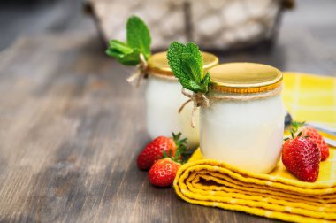 Ahşap bir masada iki bardak doğal yoğurt naneli ve çilekli..